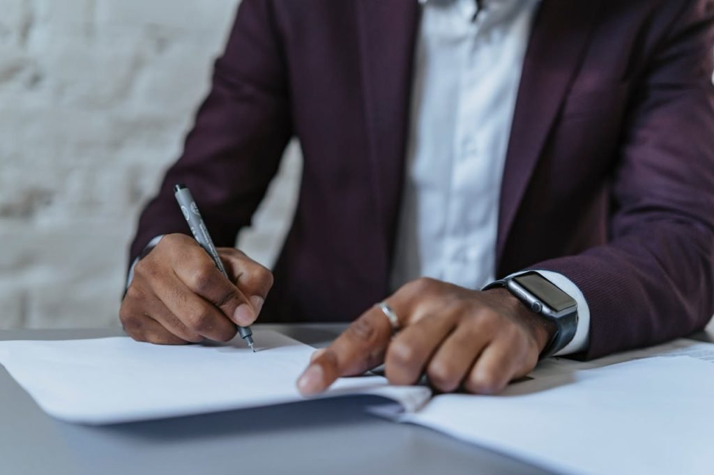a-man-writing-on-white-paper-using-a-black-pen-5313169 Close-up of a man signing documents in an office. Business-focused and professional environment.
